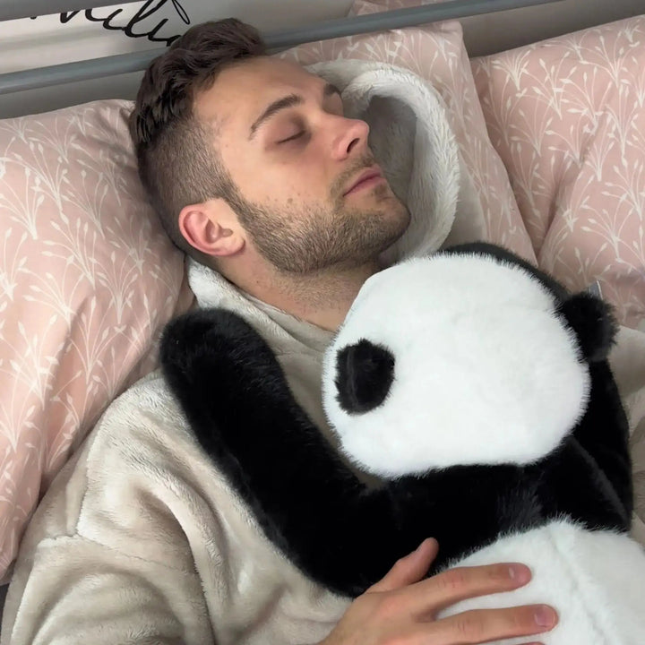 Homme endormi dans un lit aux draps rose pâle, serrant contre lui un panda en peluche dont le bras noir lui entoure l'épaule. 11