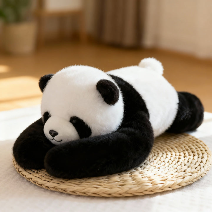 Panda en peluche noir et blanc allongé sur un set de table en paille tressée, longs bras repliés devant le museau. 1