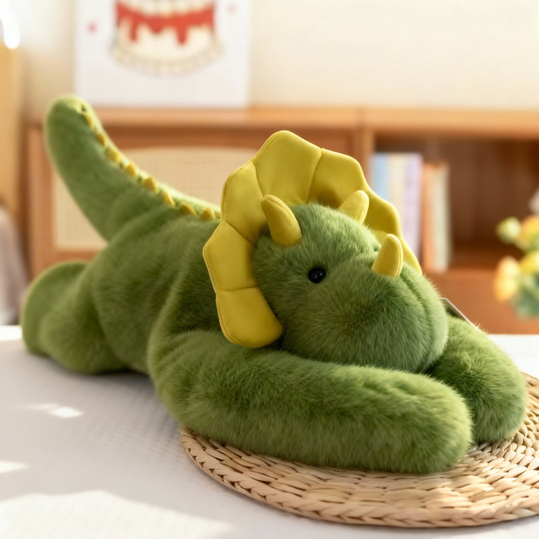 Dragon en peluche vert à collerette et cornes jaunes, allongé sur un set de table en paille, longs bras verts repliés devant lui. 15