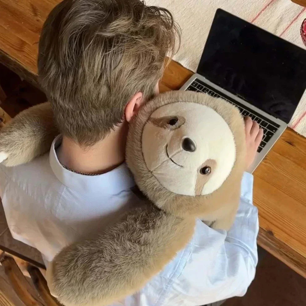 Vue de dessus d'un homme travaillant sur son ordinateur portable, un paresseux en peluche brun clair lui enlaçant les épaules. 9