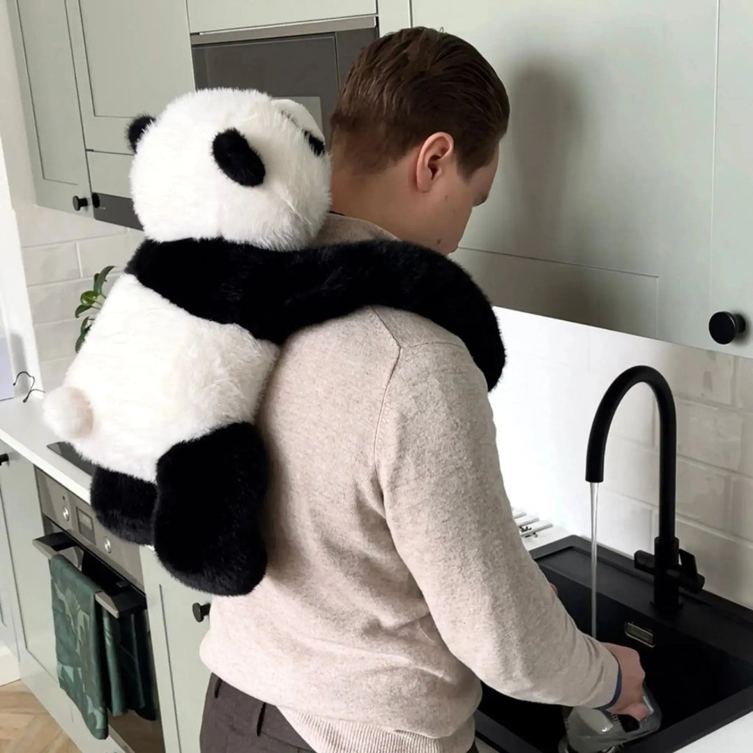 Homme faisant la vaisselle à l'évier de la cuisine, le panda en peluche accroché dans son dos avec ses bras autour du cou. 10
