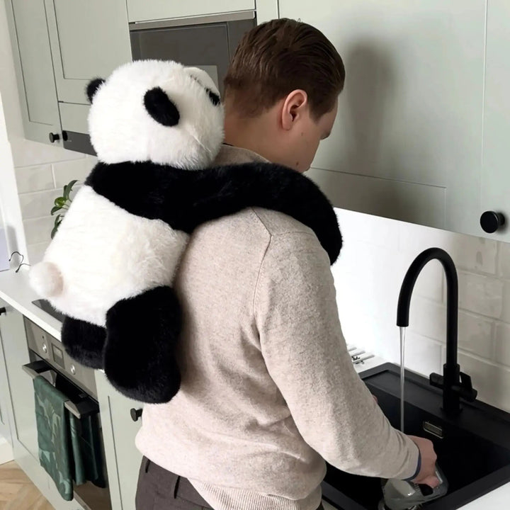 Homme faisant la vaisselle à l'évier de la cuisine, le panda en peluche accroché dans son dos avec ses bras autour du cou. 10