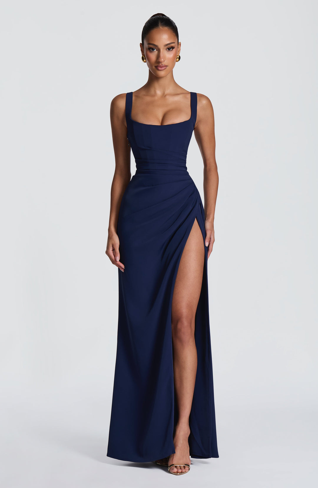 Robe bleu marine portée de face, bras le long du corps, fente haute dégageant la jambe et sandales dorées. 15