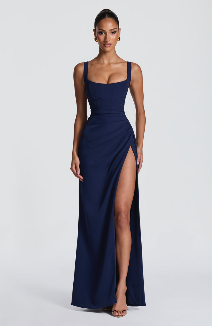 Robe bleu marine portée de face, bras le long du corps, fente haute dégageant la jambe et sandales dorées. 15