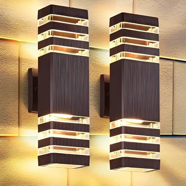 Gros plan sur deux appliques rectangulaires allumées contre un mur en pierre, avec leur lumière dorée qui éclaire la façade. 3
