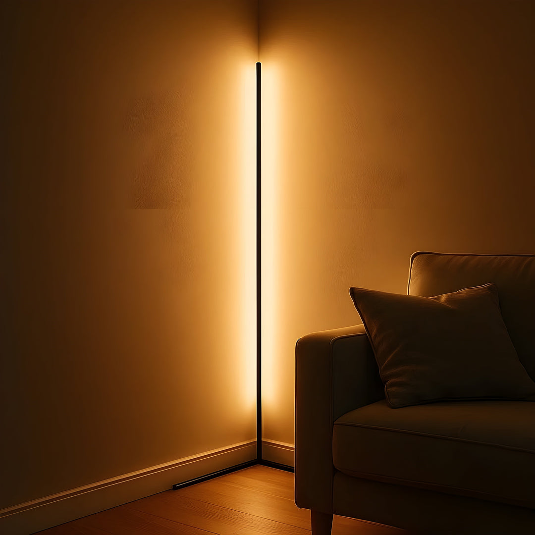 Lampadaire d'angle allumé dans la pénombre, lumière dorée diffusée sur les deux murs, accoudoir de canapé et coussin au premier plan. 3