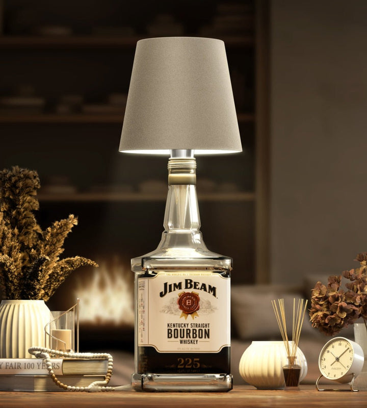 Abat-jour beige sur une bouteille carrée de bourbon, dans un salon cosy avec cheminée, bougies et fleurs séchées. 8