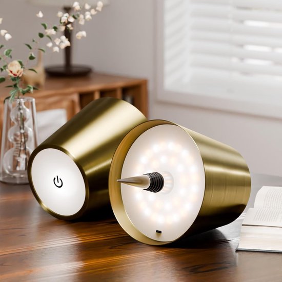 Deux abat-jours dorés couchés sur une table en bois, l'un montrant sa base tactile, l'autre son bouchon et ses LED. 9
