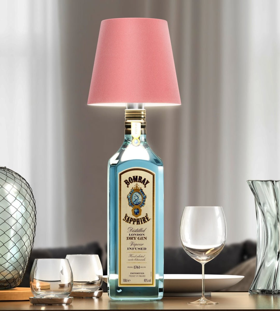 Abat-jour rose monté sur une bouteille de gin bleue, entouré de verres sur une table de salon. 4