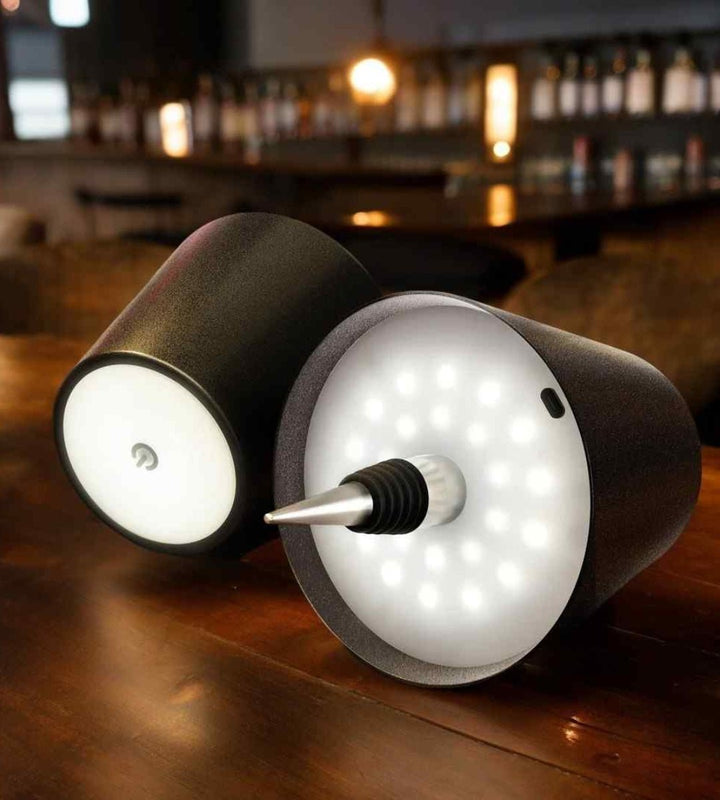 Deux lampes noires couchées sur un comptoir de bar, avec bouchon conique et disque de LED allumées visible. 10