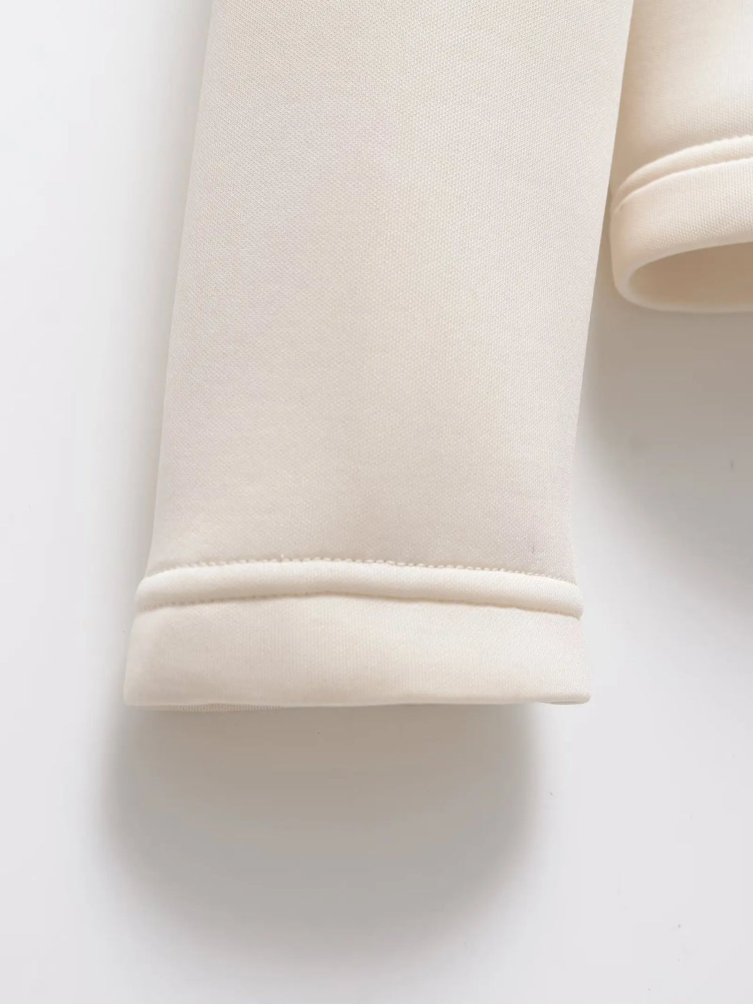 Détail du bas de manche écru posé à plat, avec sa couture et son ourlet doublé. 5