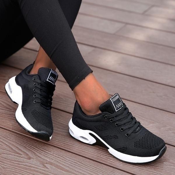 Baskets noires en maille respirante à semelle blanche avec bulle d'air, portées avec un legging noir, assise sur une terrasse en bois. 3