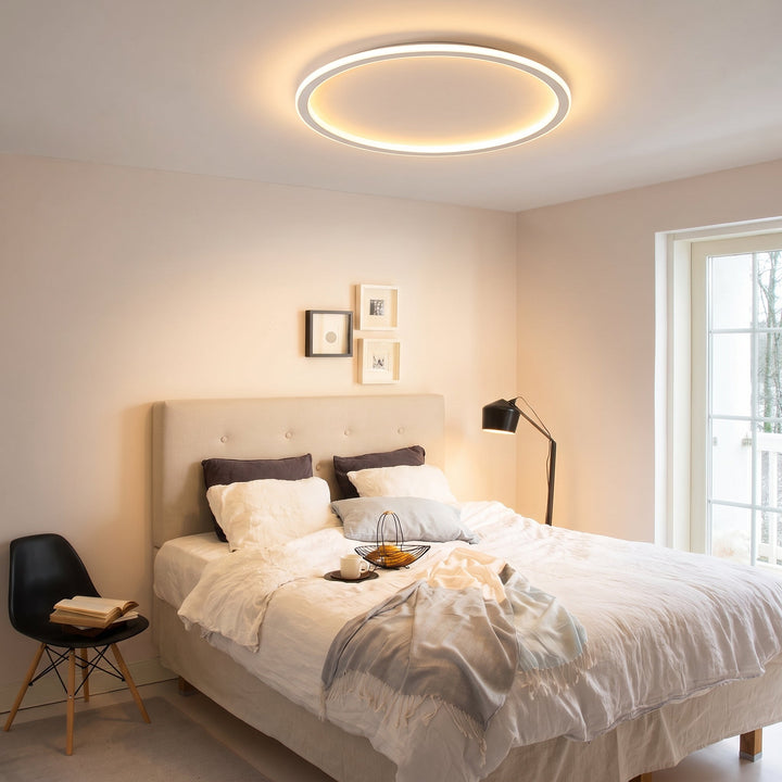 Plafonnier annulaire allumé au-dessus d'un lit aux draps blancs dans une chambre claire avec lampadaire noir. 9