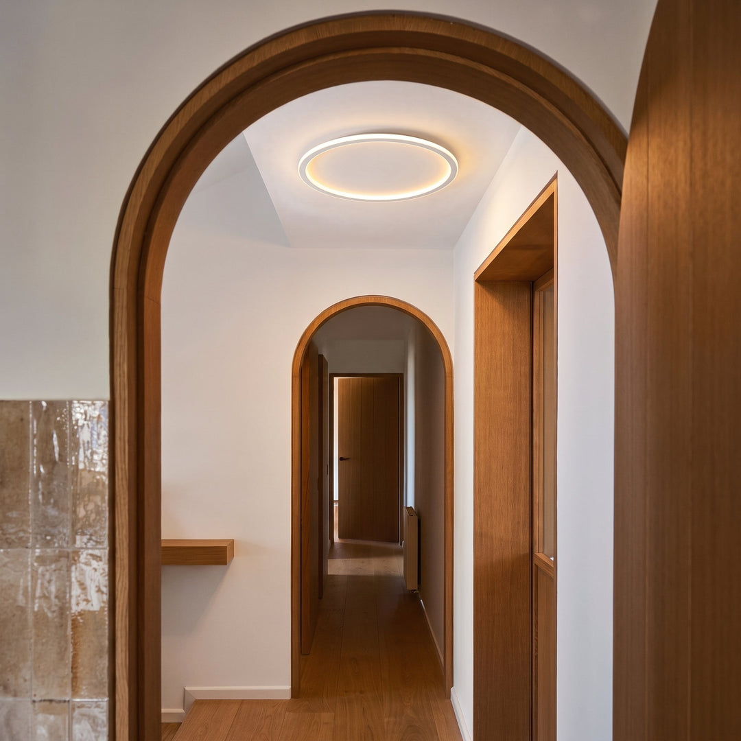 Plafonnier rond allumé au plafond d'un couloir blanc encadré d'arches en bois clair. 4