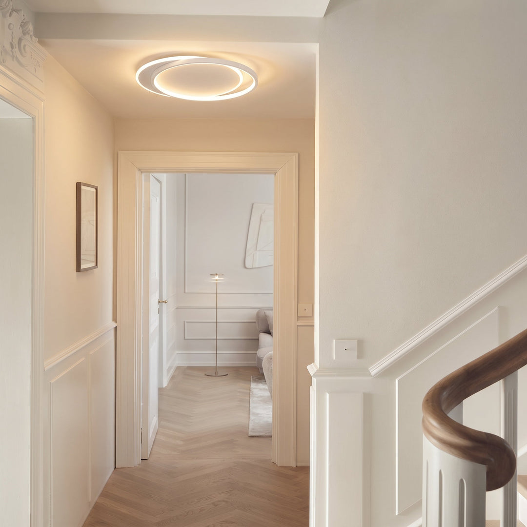 Luminaire à anneaux dans un couloir lumineux à boiseries blanches, escalier et salon au fond 7