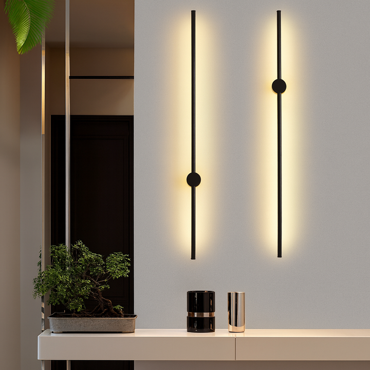 Deux appliques noires verticales allumées sur un mur gris, au-dessus d'une console blanche avec un bonsaï et deux vases. 2