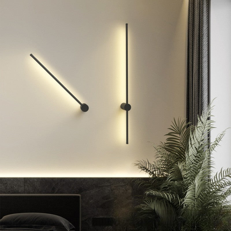 Deux appliques noires allumées, l'une inclinée en diagonale et l'autre verticale, sur un mur crème au-dessus d'une tête de lit. 5