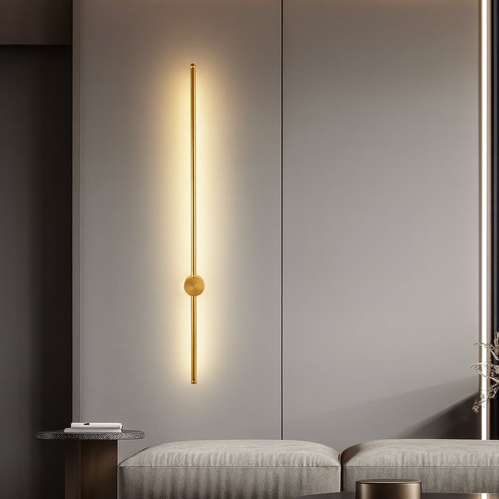 Applique dorée verticale allumée sur un mur gris, avec lumière chaude diffuse, au-dessus d'un canapé gris et d'une table d'appoint. 9