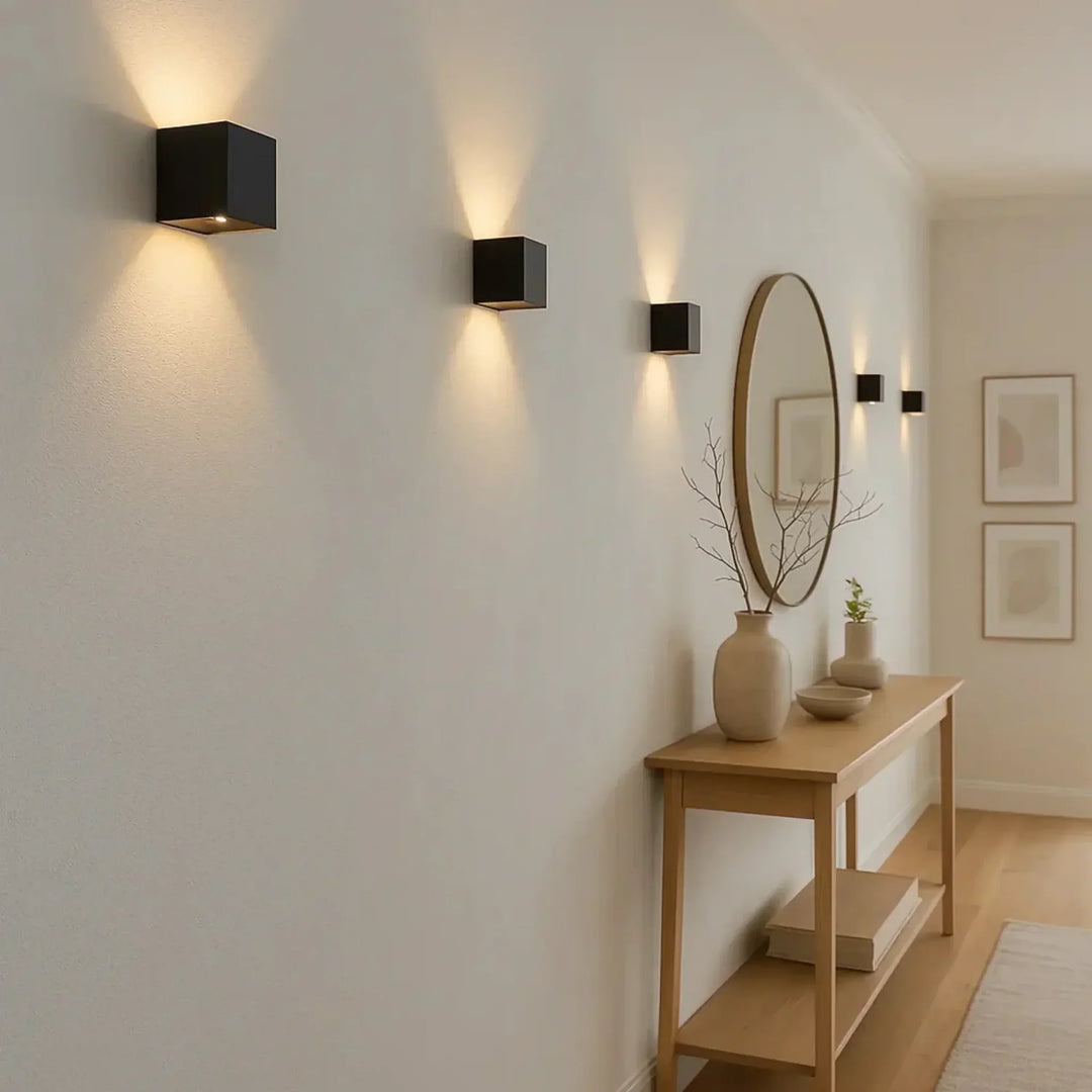 Cinq appliques cubiques noires alignées sur un mur blanc d'entrée, avec console en bois et miroir rond 3