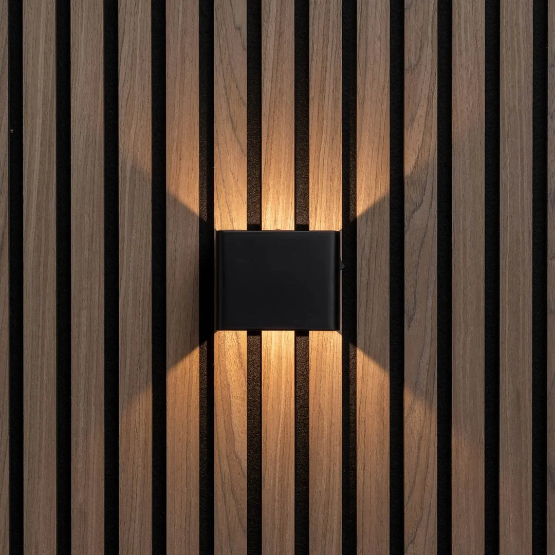Applique cubique noire vue de face, diffusant une lumière chaude vers le haut et le bas sur des lattes de bois 5