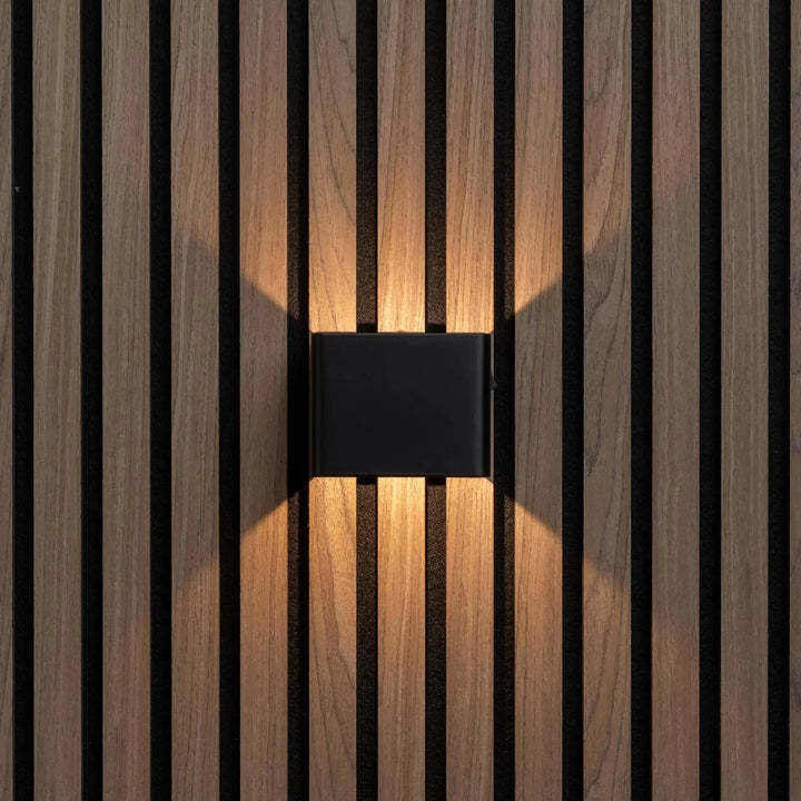 Applique cubique noire vue de face, diffusant une lumière chaude vers le haut et le bas sur des lattes de bois 5