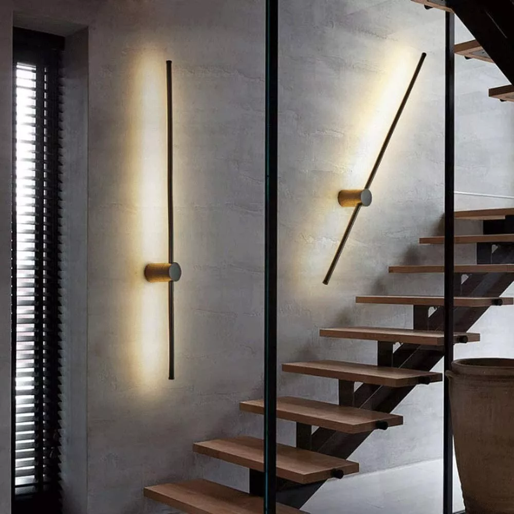 Deux appliques en barre, l'une verticale et l'autre inclinée, sur un mur de béton gris près d'un escalier aux marches en bois. 4