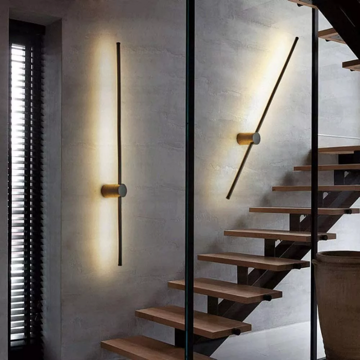 Deux appliques en barre, l'une verticale et l'autre inclinée, sur un mur de béton gris près d'un escalier aux marches en bois. 4