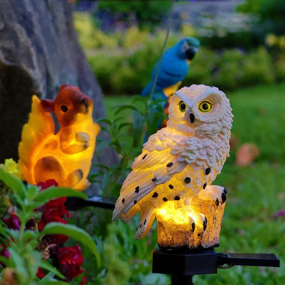Hibou blanc allumé au premier plan dans un massif fleuri, à côté d'un écureuil lumineux et d'un perroquet bleu décoratifs. 12