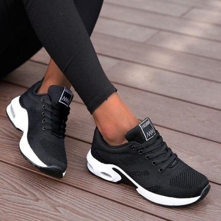Baskets noires en maille aérée à semelle blanche avec bulle d'air, portées avec un legging noir sur une terrasse en bois. 1