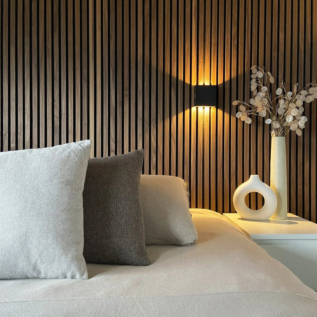 Applique cubique noire fixée sur un mur de tasseaux en bois, au-dessus d'une table de chevet avec vases blancs et coussins. 5