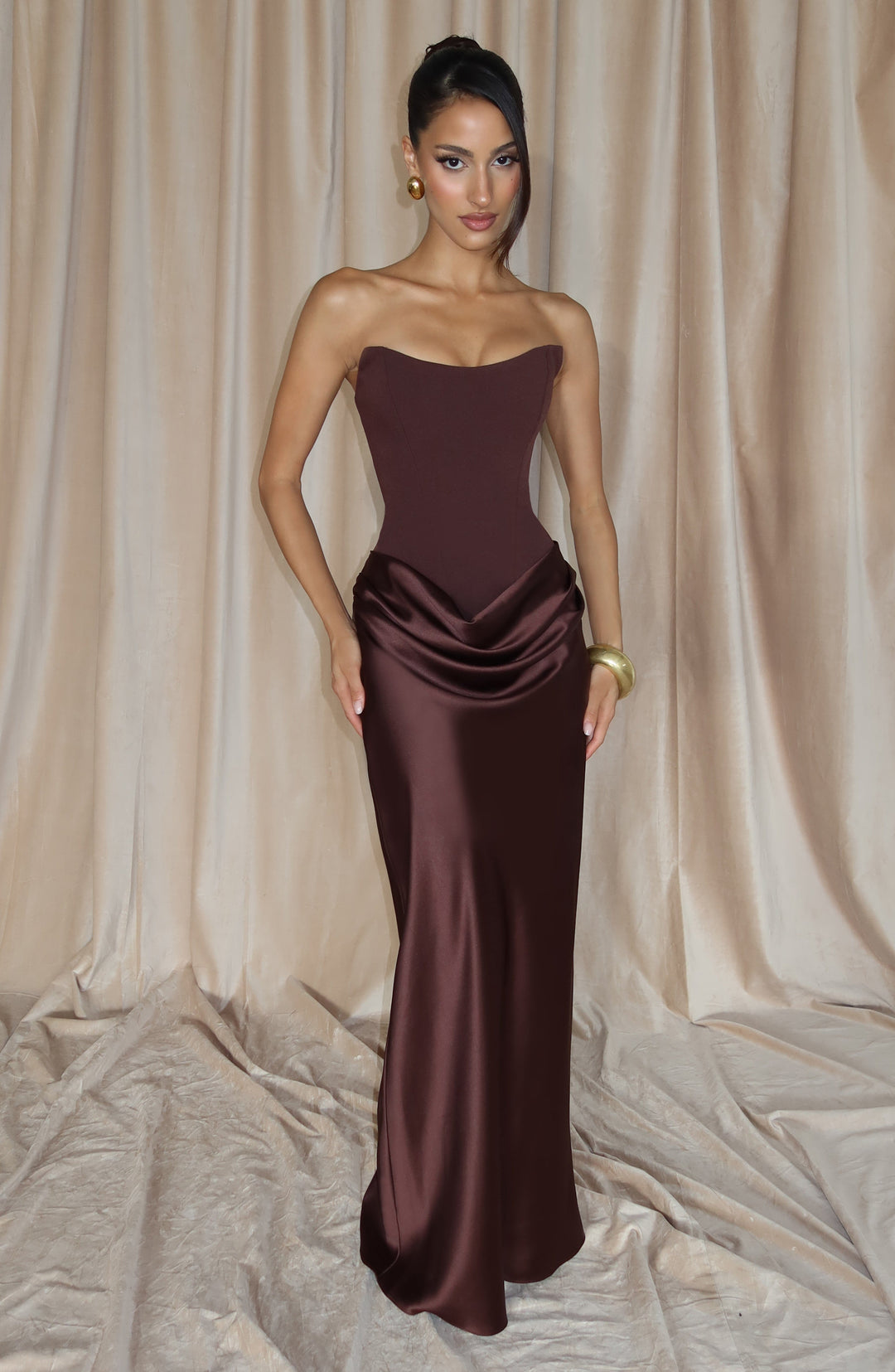 Mannequin en robe marron devant un rideau beige, main sur la hanche, bracelet doré 8