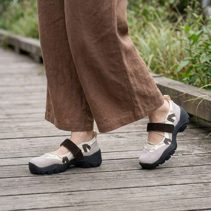 Chaussures beige clair à bride marron foncé portées sur une passerelle en bois, avec un pantalon ample en lin marron. 11