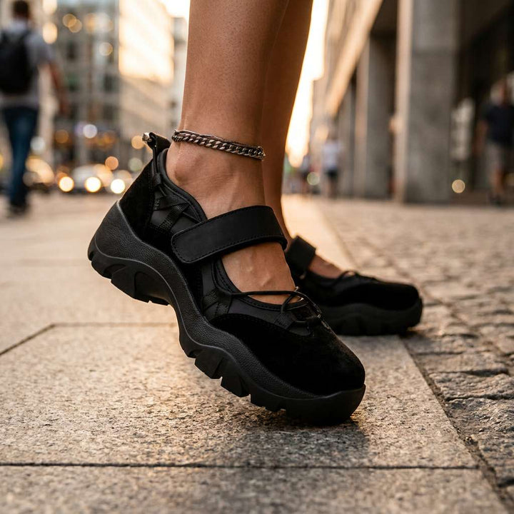 Chaussures noires à semelle plateforme portées sur un trottoir en pierre, avec une chaîne de cheville argentée visible. 13