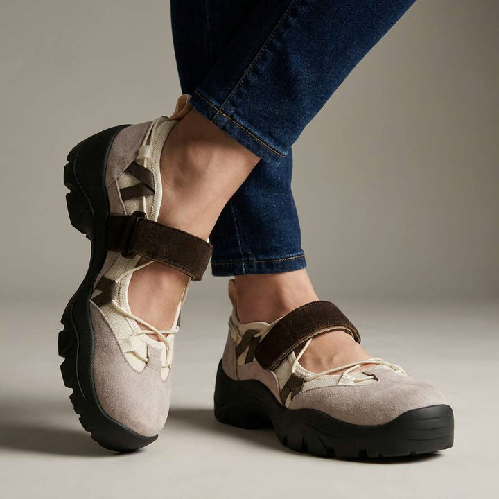 Chaussures beige et blanc cassé à bride marron et semelle noire crantée, portées avec un jean brut sur fond neutre. 1