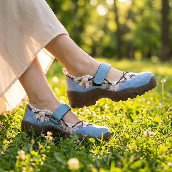 Chaussures bleues à semelle marron et détails à carreaux portées dans l'herbe fleurie, avec une jupe longue crème. 8