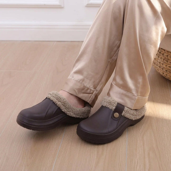 Pieds portant des sabots marron à doublure fourrée, avec legging gris, posés sur un parquet clair 10