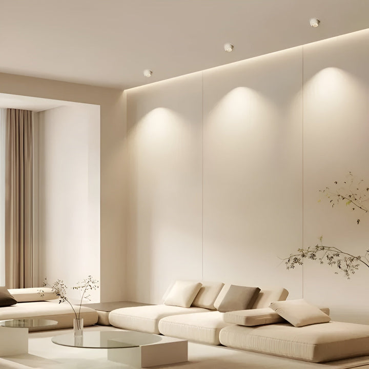 Trois spots blancs encastrés au plafond d'un salon beige, projetant des cônes de lumière chaude sur le mur 2