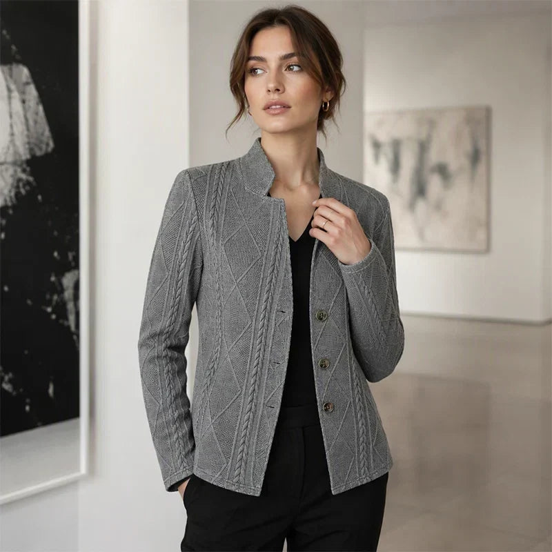 Femme dans une galerie, portant le blazer gris texturé ouvert sur un haut noir, une main dans la poche du pantalon. 11