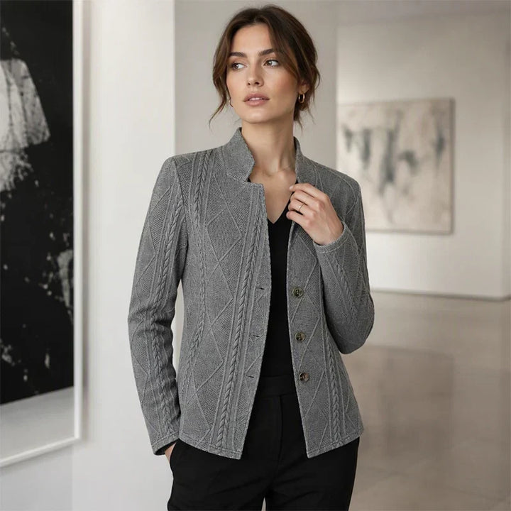 Femme dans une galerie, portant le blazer gris texturé ouvert sur un haut noir, une main dans la poche du pantalon. 11