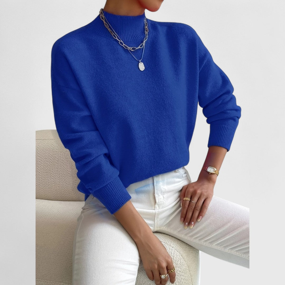 Pull bleu roi à col montant et manches longues, porté avec un pantalon blanc, collier argenté et montre dorée. 11