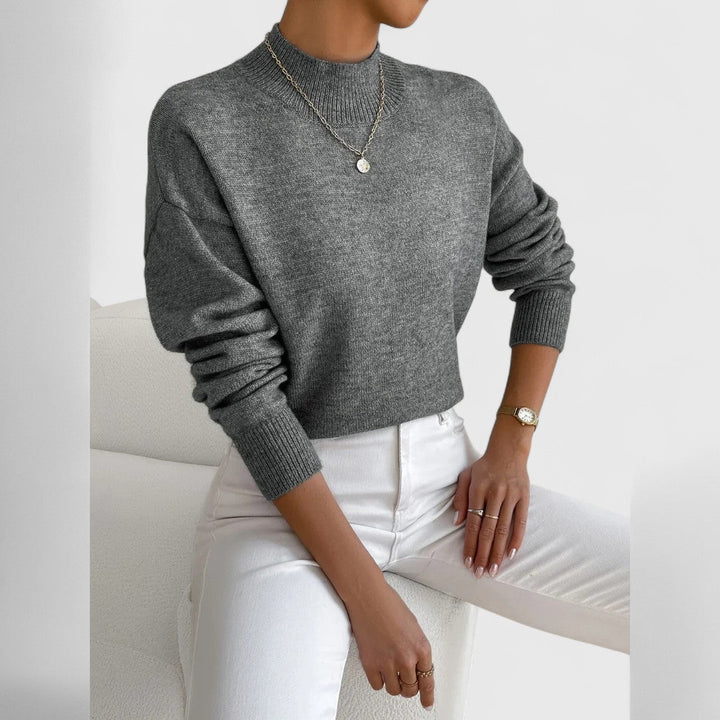 Pull gris chiné à col montant et poignets côtelés, porté avec un pantalon blanc et un fin collier à médaille. 12