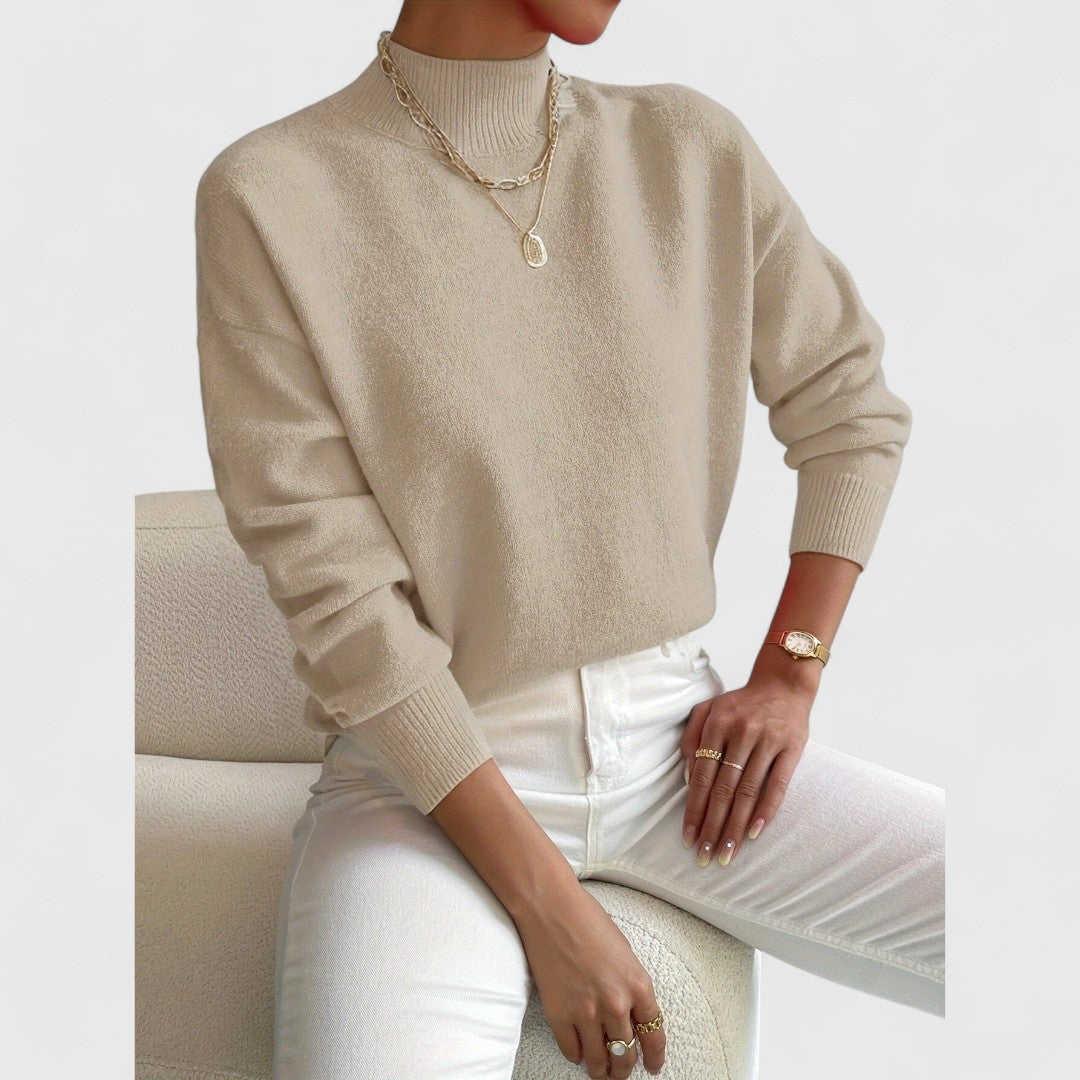 Pull beige sable à col montant porté avec un pantalon blanc, collier doré et fauteuil bouclé crème. 7
