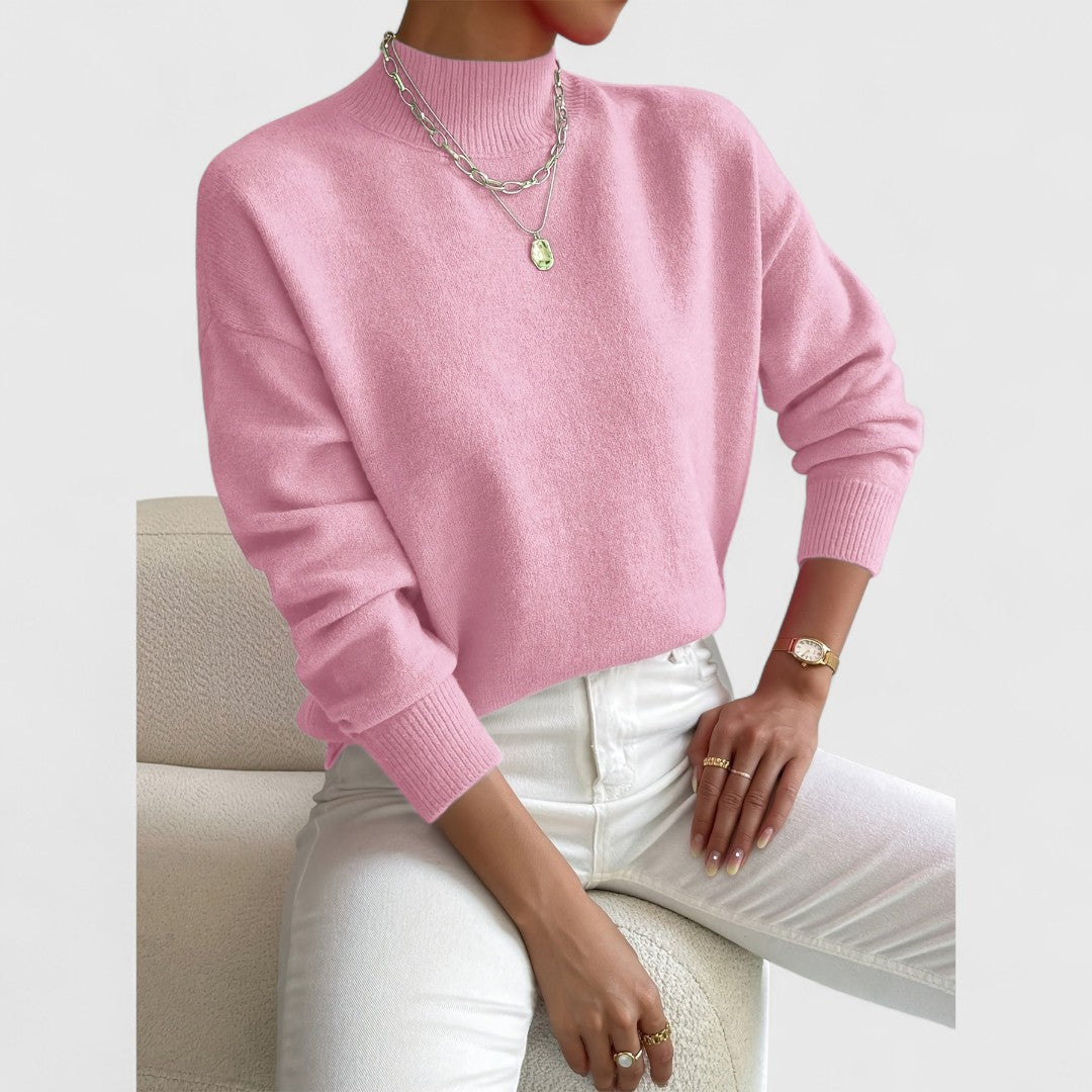 Pull rose bonbon à col montant et poignets côtelés, porté avec un pantalon blanc, assise sur un fauteuil bouclé. 5