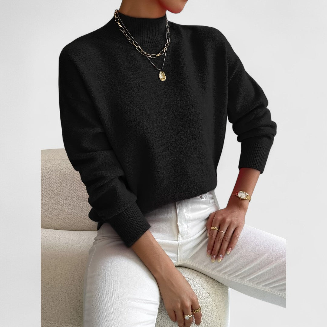 Pull noir à col montant et poignets côtelés, porté avec un pantalon blanc, collier doré et montre au poignet. 8