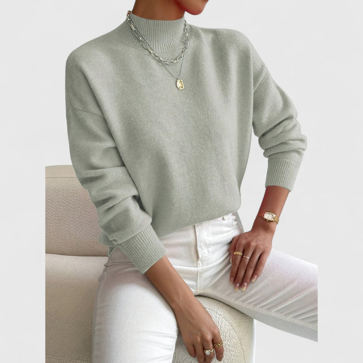 Pull vert sauge porté en plan légèrement plus serré, manches longues, collier doré et montre au poignet, pantalon blanc. 3