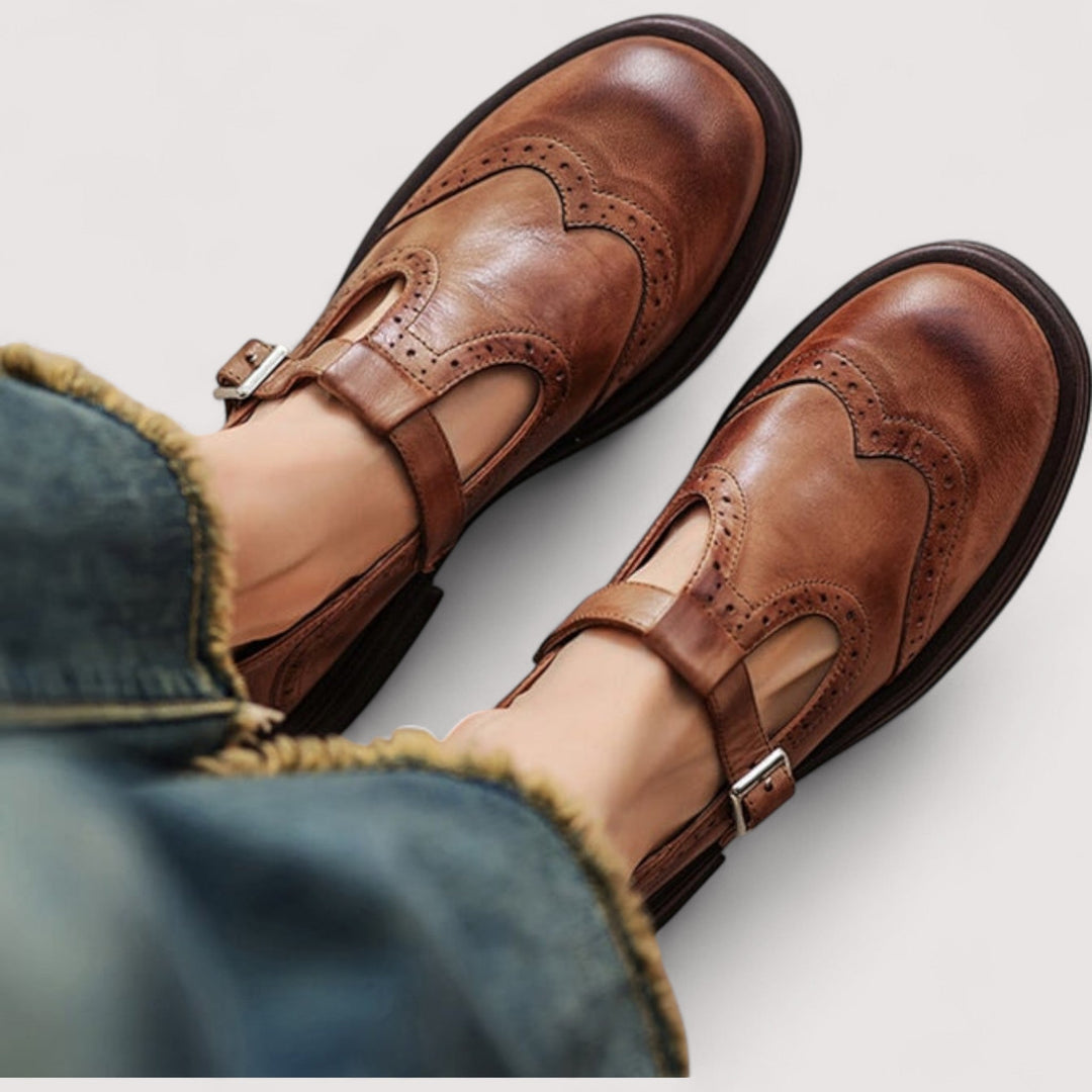 Vue de dessus de pieds portant les babies en cuir brun nuancé à bride bouclée et perforations, avec un jean frangé. 1