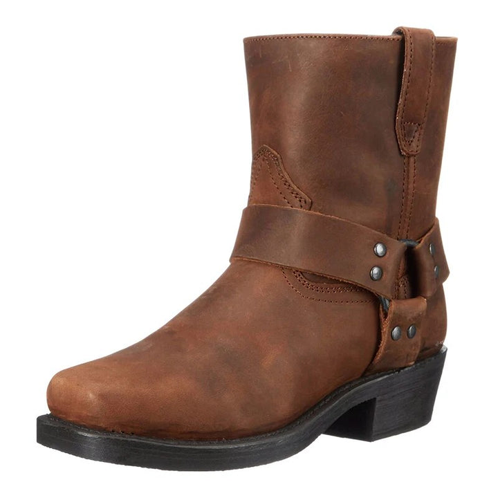 Botte en cuir marron vue de trois quarts, avec sangle cloutée autour de la cheville, bout carré et talon bas. 1