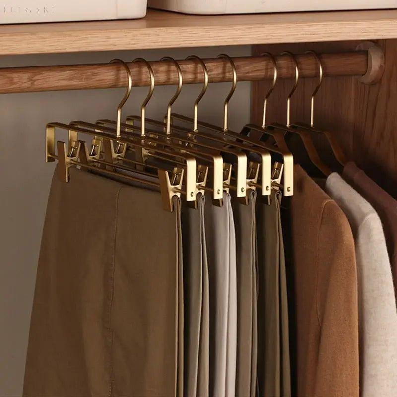 Plusieurs cintres dorés à pinces suspendus à une tringle en bois, avec pantalons dans une penderie 3