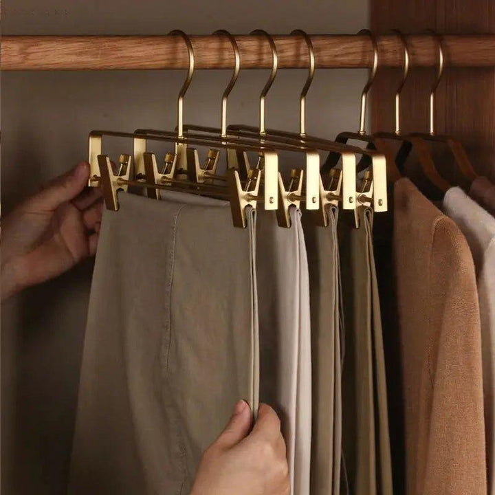 Main accrochant des pantalons sur des cintres dorés à pinces alignés sur une tringle en bois 7