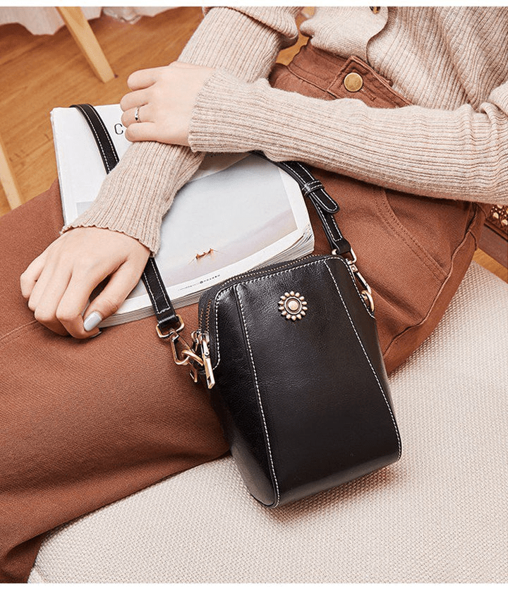 Sac noir porté en bandoulière par une femme assise en pull beige, posé près d'un magazine 9